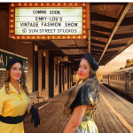 Two sisters on a train platform, dressed in 1950s vintage clothing. A vintage train has arrived. A sign announces th upcoming event. 